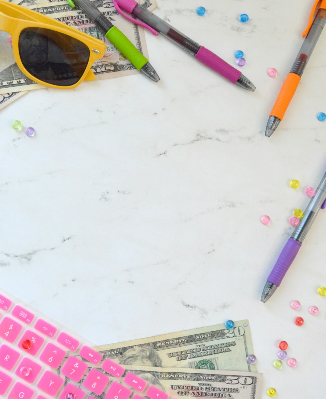 Marble money styled stock photo and money flat lay photo for personal finance bloggers, business coaches, and entrepreneurs with a pink keyboard, sunglasses, colorful pens, and more.